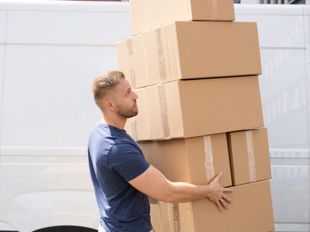A man and van in blue-shirt with a pile of moving boxes outside the white van