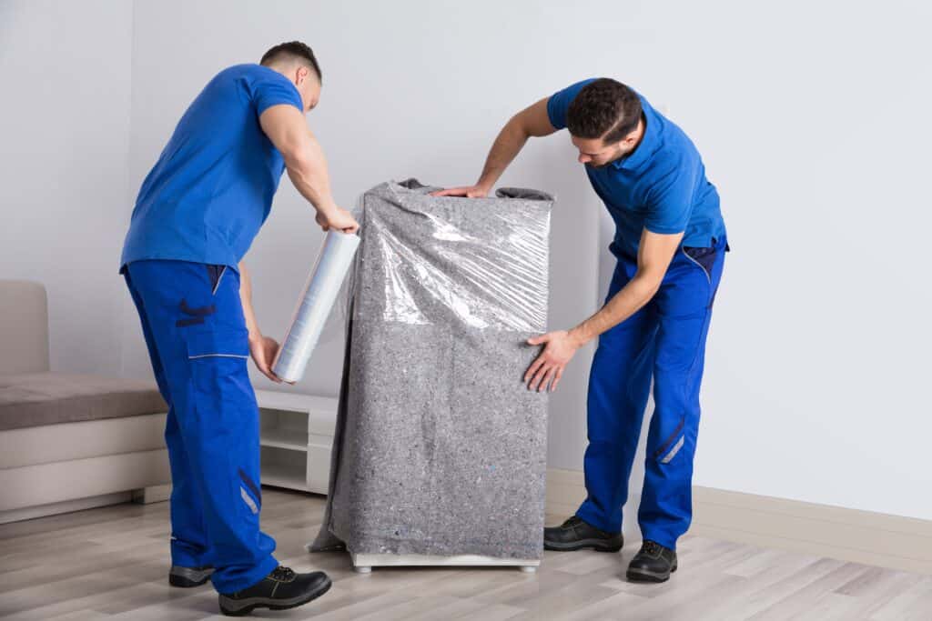 Two movers wrapping a cabinet on a moving day